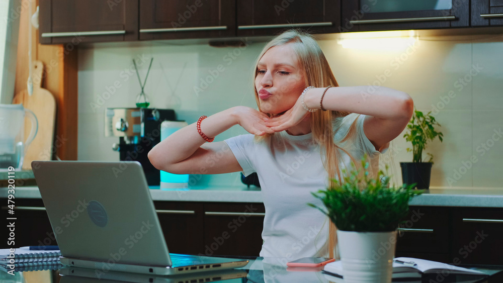 Cheerful woman singing and gesturing while looking on the computer screen. She spending her free time in the kitchen. Cheerful woman singing and gesturing while looking on the computer screen. She spending her free time in the kitchen.