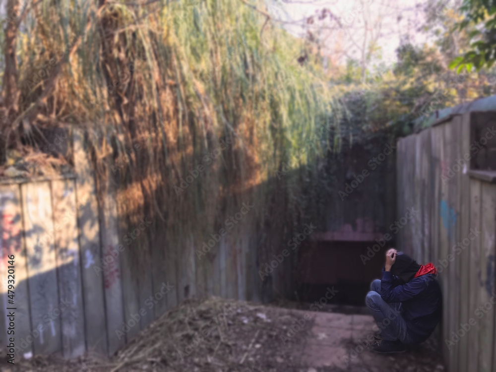 The young man in hat and jacket sitting on the staircase that lead to the underground passage. Deep in thought. Mental health concept. Side view of the man with depressed emotion over trouble and prob The young man in hat and jacket sitting on the staircase that lead to the underground passage. Deep in thought. Mental health concept. Side view of the man with depressed emotion over trouble and prob