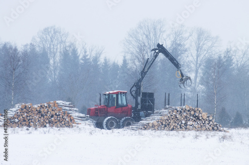 Obraz na plátně A red wood forwarder unloading timber to a wood pile on a cold winter day in Estonia, Northern Europe