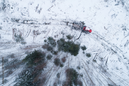 An aerial view of a small clear-cut area after deforestation with a red forwarder collecting timber on winter day in European forest, Estonia. 