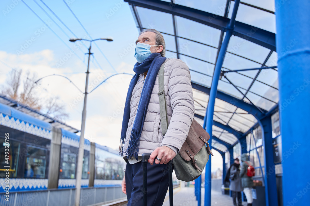 Male person with mask at his face looking at the distance while waiting for his train Male person with mask at his face looking at the distance while waiting for his train