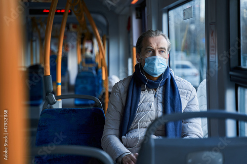 Mature male person in protective mask wearing earphones listening music