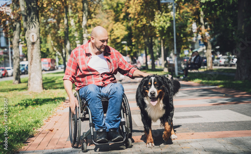 Happy young man with a physical disability who uses wheelchair with his dog. © romaset