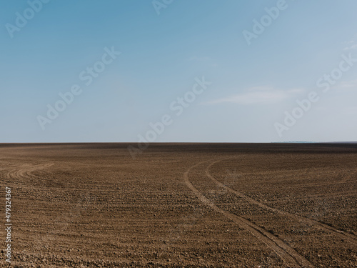 brown field under blue sky with wheel tracks on it
