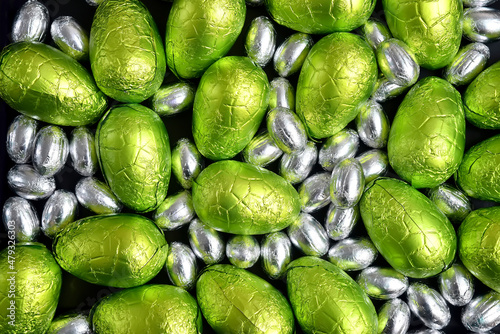 Large & small green, lime green and silver spring colours of foil wrapped chocolate easter eggs, against a black background.