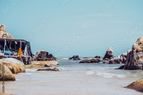 Real nature beauty view background. Sea ocean huge rocks stones coast bay landscape sun day blue sky, pale brown orange yellow boulders. Sailor hut with simple life style fishing gear. Vacation travel