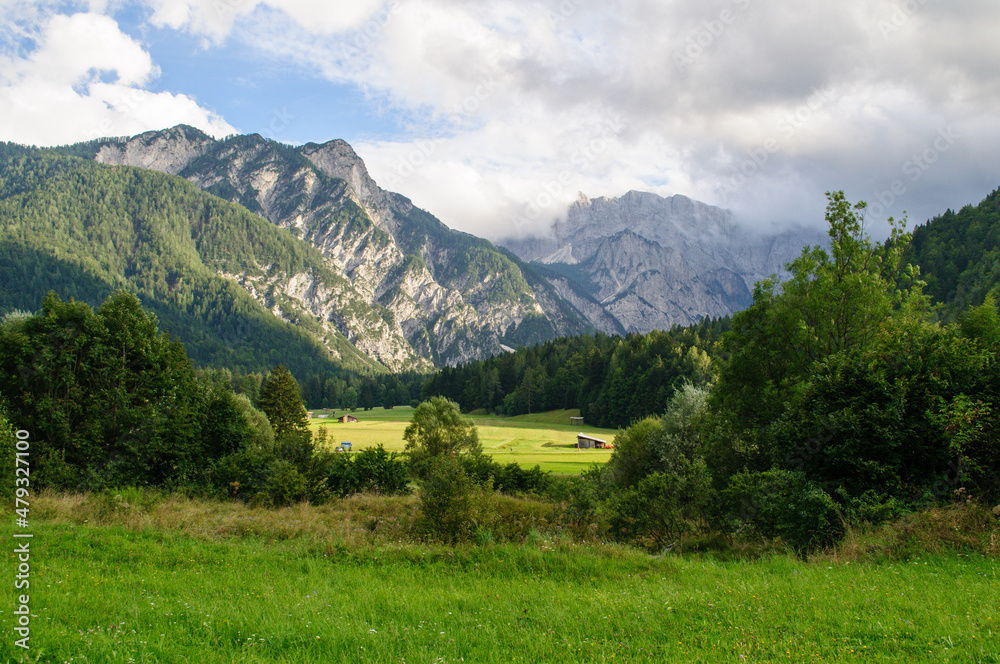 High rocky mountains in summer, blue sky and green forests with grassy meadow in Slovenia.