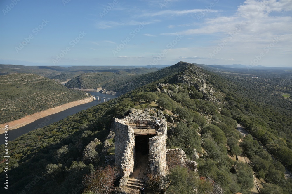 Ruins of Monfragüe castle stone tower, the river Tajo reservoir with El Cardenal bridge and the typical central Spanish arid oak dehesa of Monfragüe National Park in the background