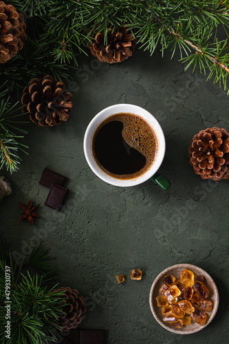 Black coffee in a green cup  chocolate and caramel sugar on a green background with fir branches and cones. Top view