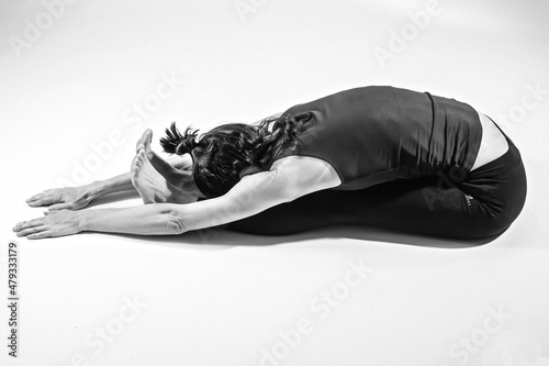 black and white image of the dancer doing a forward bend while sitting on the floor of the dance studio with her legs straight 