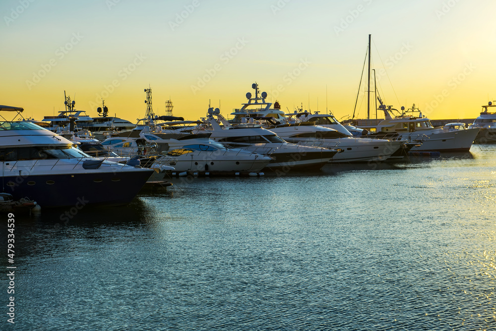 Luxury yachts docked in sea port at sunset. Marine parking of modern motor boats and blue water. Tranquility, relaxation and fashionable vacation