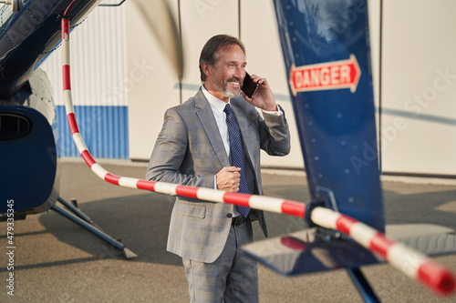 Fotografia Joyous businessman talking on smartphone beside rotorcraft
