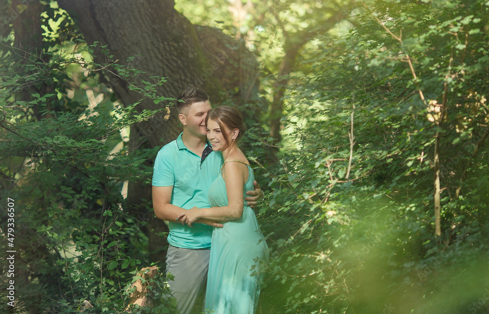 a young man and a pregnant woman are standing in the forest and laughing. Green clothes a young man and a pregnant woman are standing in the forest and laughing. Green clothes