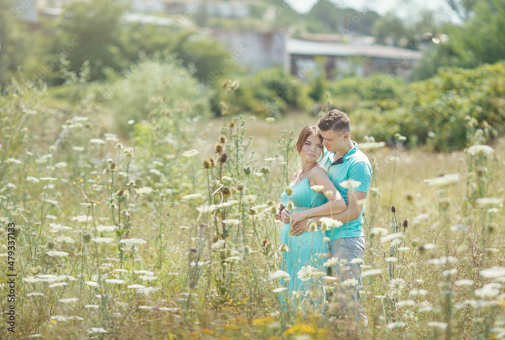 Naklejka premium a beautiful pregnant girl and a guy are standing in a field in the greenery and having fun. green clothes.