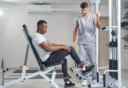 Focused male patient doing strength training exercise supervised by physiatrist