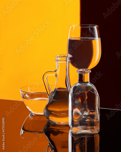 Various glassware with water on a colorful background. The dishes are on a glossy surface.
