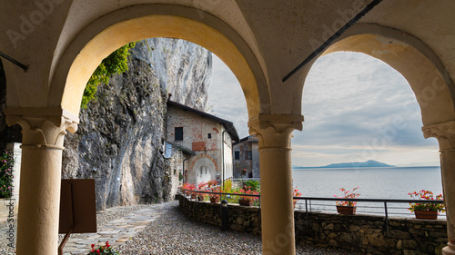 Arcades in the famous "Eremo di Santa Caterina del Sasso" (meaning: "Saint Catherine of the stone hermitage"). Blue waters of Lake Maggiore on the right, with cloudy sky, Italy.