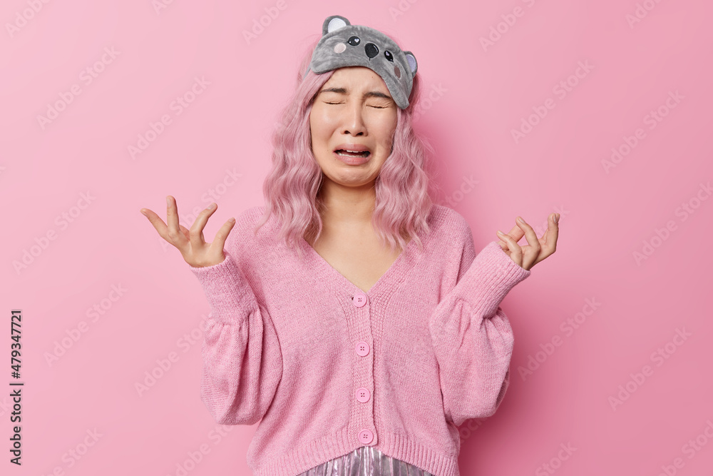 Upset frustrated doleful woman raises hands feels disappointed cries from despair looses control wears sleepmask and jumper isolated over pink background. Negative emotions and feelings concept Upset frustrated doleful woman raises hands feels disappointed cries from despair looses control wears sleepmask and jumper isolated over pink background. Negative emotions and feelings concept
