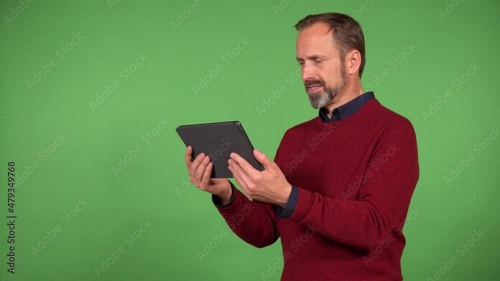 A middle-aged handsome Caucasian man looks at a tablet with a smile - green screen background A middle-aged handsome Caucasian man looks at a tablet with a smile - green screen background
