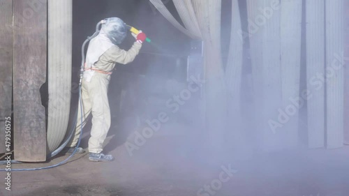 The sandblaster in protective suit and helmet is sandblasting new metal construction. High quality 4k footage photo