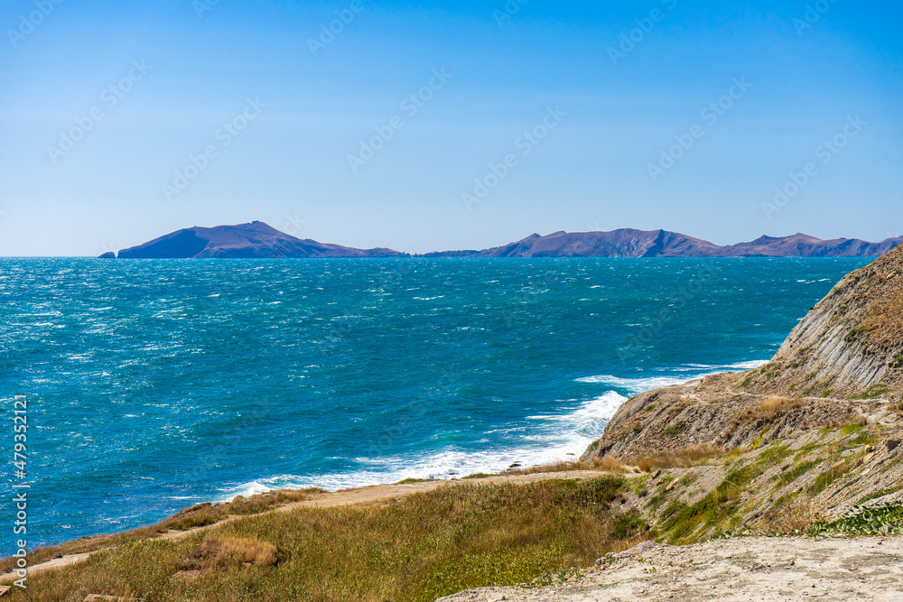 Fototapeta premium Picturesque summer landscape of sea coast with waves on water surface against mountains and sky. Beautiful seascape in sunny day, natural background. Feodosia vicinity, Crimea, Russia
