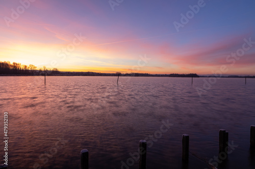 Early winter morning during sunrise and the light reflects over the water of the lake and creates a fairy tale landscape full of colors together with the frozen water and a veil of mist