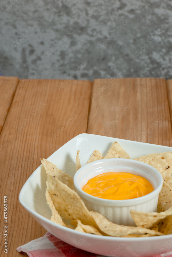 Cheddar on a bowl of nachos on a wooden table. The background is grey. Vertical image Cheddar on a bowl of nachos on a wooden table. The background is grey. Vertical image
