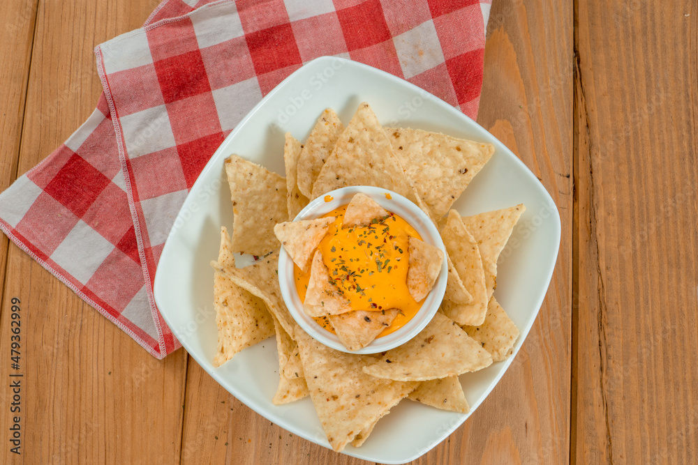 Nachos dipped in cheddar on a bowl on a wooden table. Under the dish there is a red and white kitchen cloth and the background is grey. Vertical image Nachos dipped in cheddar on a bowl on a wooden table. Under the dish there is a red and white kitchen cloth and the background is grey. Vertical image