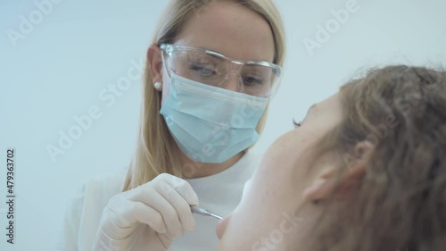 Low angle shot of Caucasian female dentist doing exam and checking up on oral health, teeth and gums of her female patient. photo