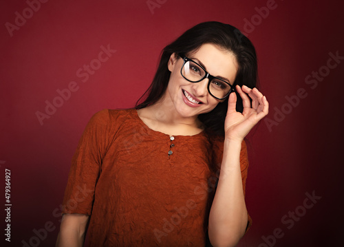 Beautiful thinking smiling happy woman  looking happy in eye glasses and holding spectacles in casual orange t-shirt on red background with empty copy space. Closeup
