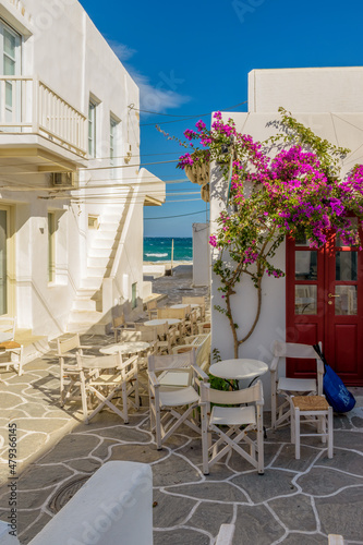 Traditional Cycladitic alley with narrow street, whitewashed facade of stores a tavern exterior and a blooming bougainvillea in Naousa Paros island, Greece.