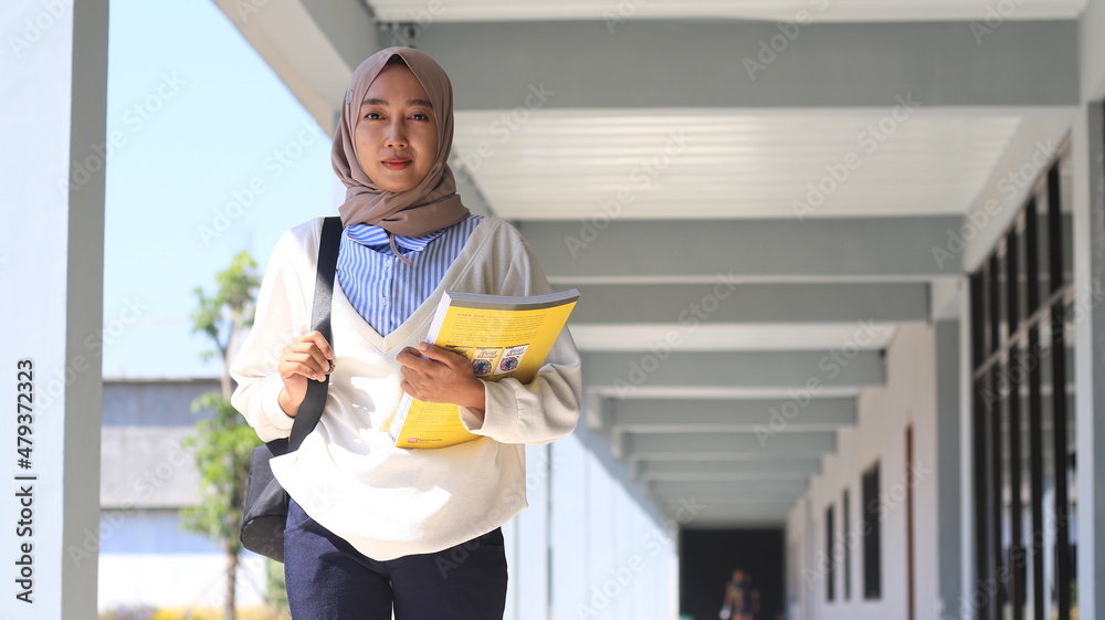 asian hijab woman student standing in the school hallway carrying a book asian hijab woman student standing in the school hallway carrying a book