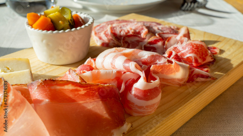 Delicious cutting board of fresh cold cuts on wooden plate. Bacon, salami coppa, speck and mix of pickled vegetables Giardiniera. Traditional Italian dish photo