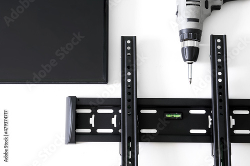 Black TV wall bracket, electric drill and monitor on a white background. The concept of mounting a TV or computer monitor on a wall. Bubble level