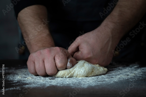 Baking fresh bread in the bakery, hands of male knead dough on kitchen table with flour