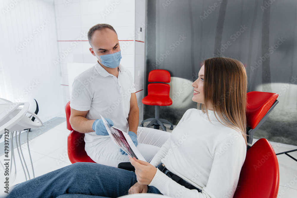 Obraz premium The dentist advises a young beautiful woman about the treatment and prosthetics of teeth in modern white stomatolgia. Dental prosthetics, treatment and teeth whitening.