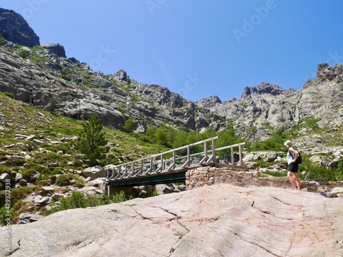 Hiker crossing wooden bridge over Golf in remote mountains on the way to Paglia Orba, Corsica, France.