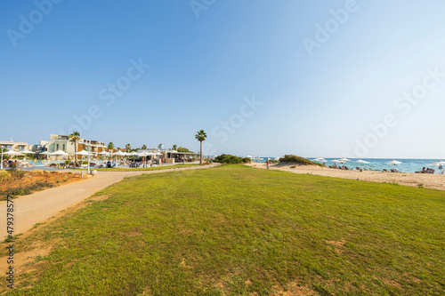 Beautiful landscape view of territory hotel building with pool and tourists on sand beach on blue sky background. Greece. 