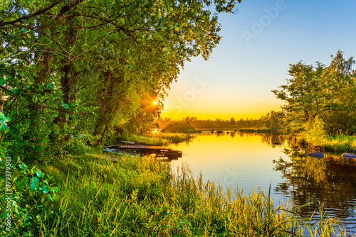 Sunset over the river. Clear sky. Overgrown coast with boats. Smooth surface of water. View from the shore. Ducks swim. Russia, Europe. © Georgii Shipin