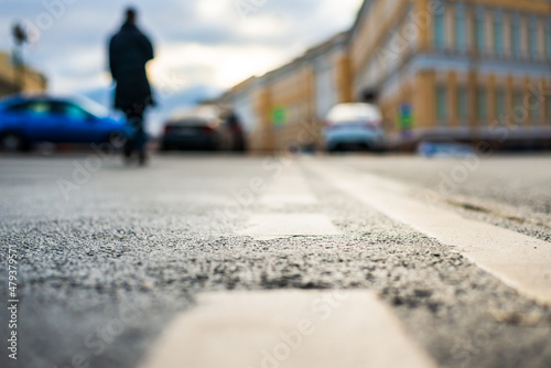 Rainy day in the city. A pedestrian is walking along the road. Historical center of the city. Focus on the asphalt. Close up view from the level of the dividing line.