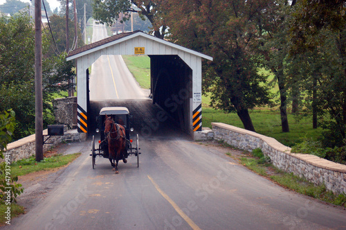 Photo An Amish horse and buggy emerge from a covered bridge as it travels the landscap