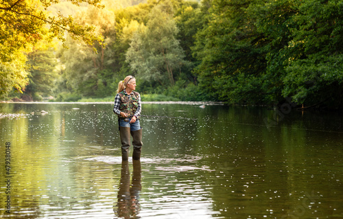 A woman stands in the river and fishes with a spinning rod