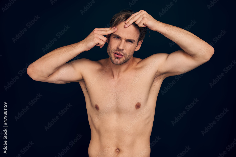 Handsome young man isolated. Portrait of shirtless muscular man is standing on dark blue background and combing out his hair