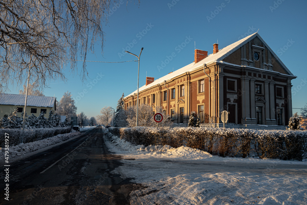 old manor house in Latvia village Vircava in winter. Straight cleaned asphalt road