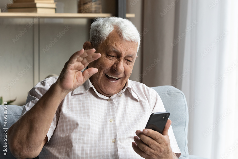 Happy elderly senior 80s retired man waving hand, looking at cellphone screen, starting web camera video call conversation with friend or grownup children, old people and modern technology usage. Happy elderly senior 80s retired man waving hand, looking at cellphone screen, starting web camera video call conversation with friend or grownup children, old people and modern technology usage.