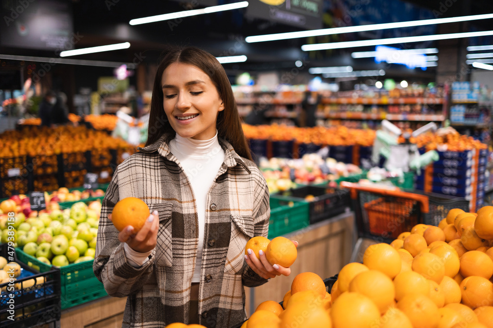 Beautiful young woman buying fresh oranges at the grocery supermarket