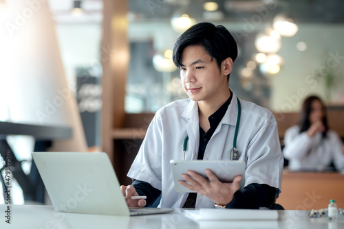 Young Asian doctor man holding tablet and printing laptop computer on work table. Free Download Young Asian doctor man holding tablet and printing laptop computer on work table. - GFXLoad