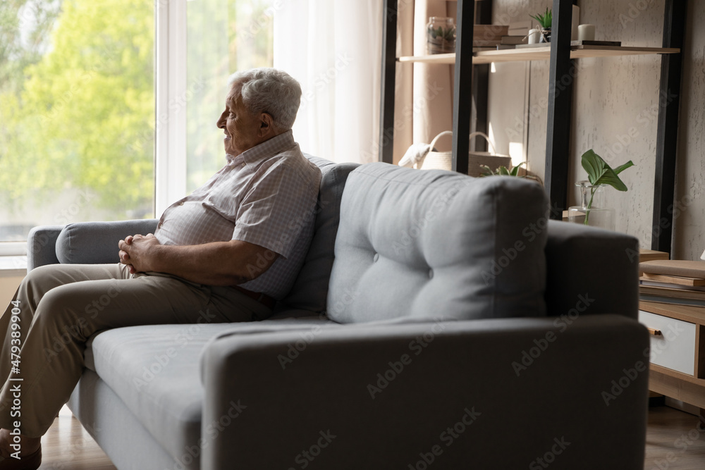Relaxed happy old 80s retired hoary man sitting on comfortable sofa, looking in distance recollecting good memories or thinking or positive life moments, enjoying carefree peaceful time, copy space.