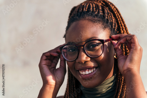 Fotografie smiling young black woman putting on her glasses