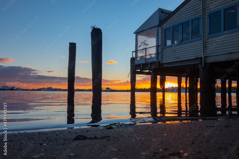 Sunrise over bay, Tauranga harbour with silhouette old posts and building at waters edge.